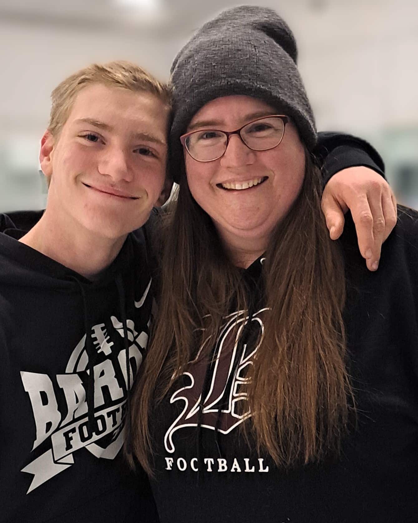 Woman in beanie with long hair posing with son in a hockey rink.